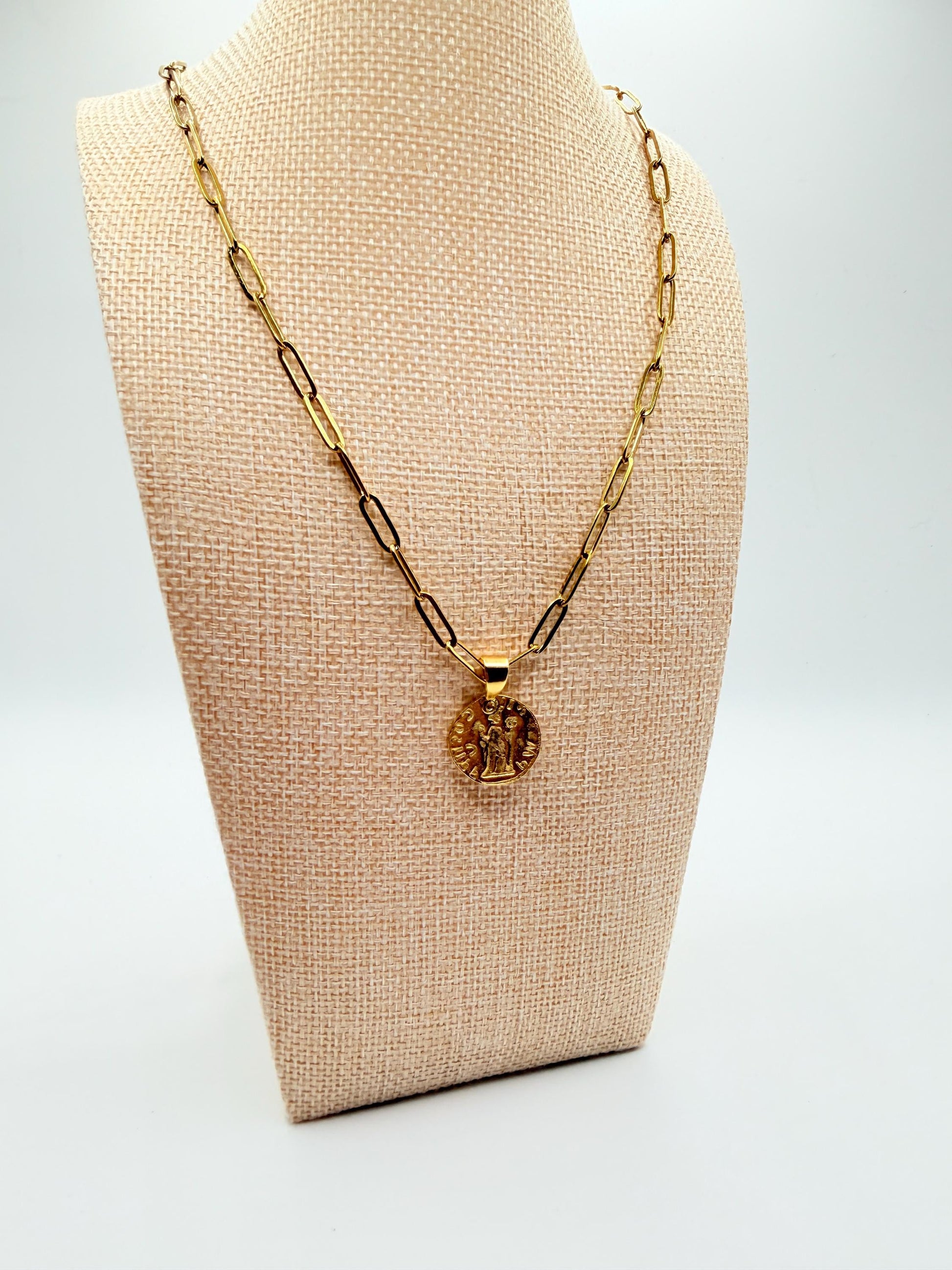 Gold necklace with a pendant on a beige bust against a white background