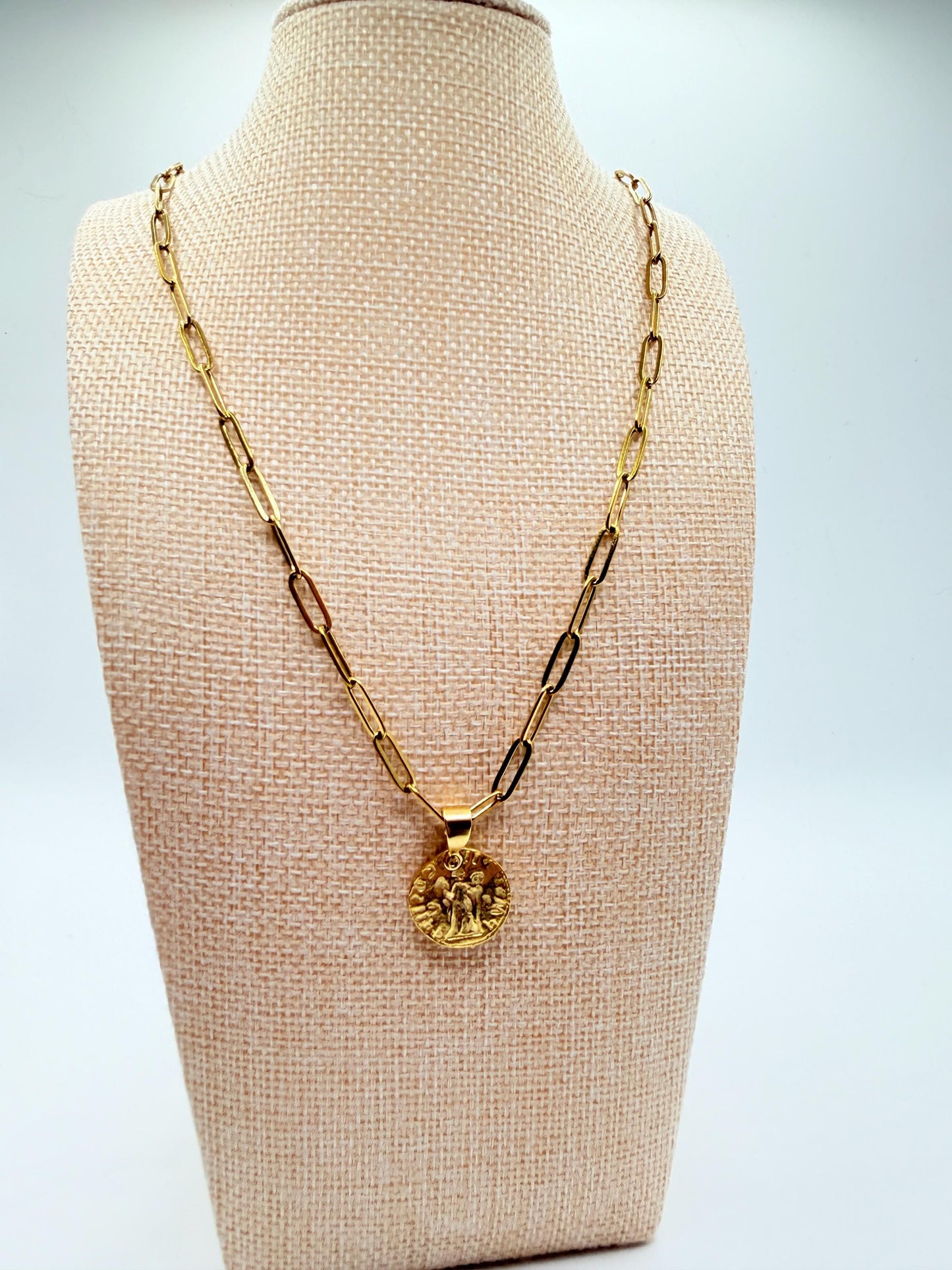 Gold necklace with a pendant on a beige mannequin bust against a light gray background