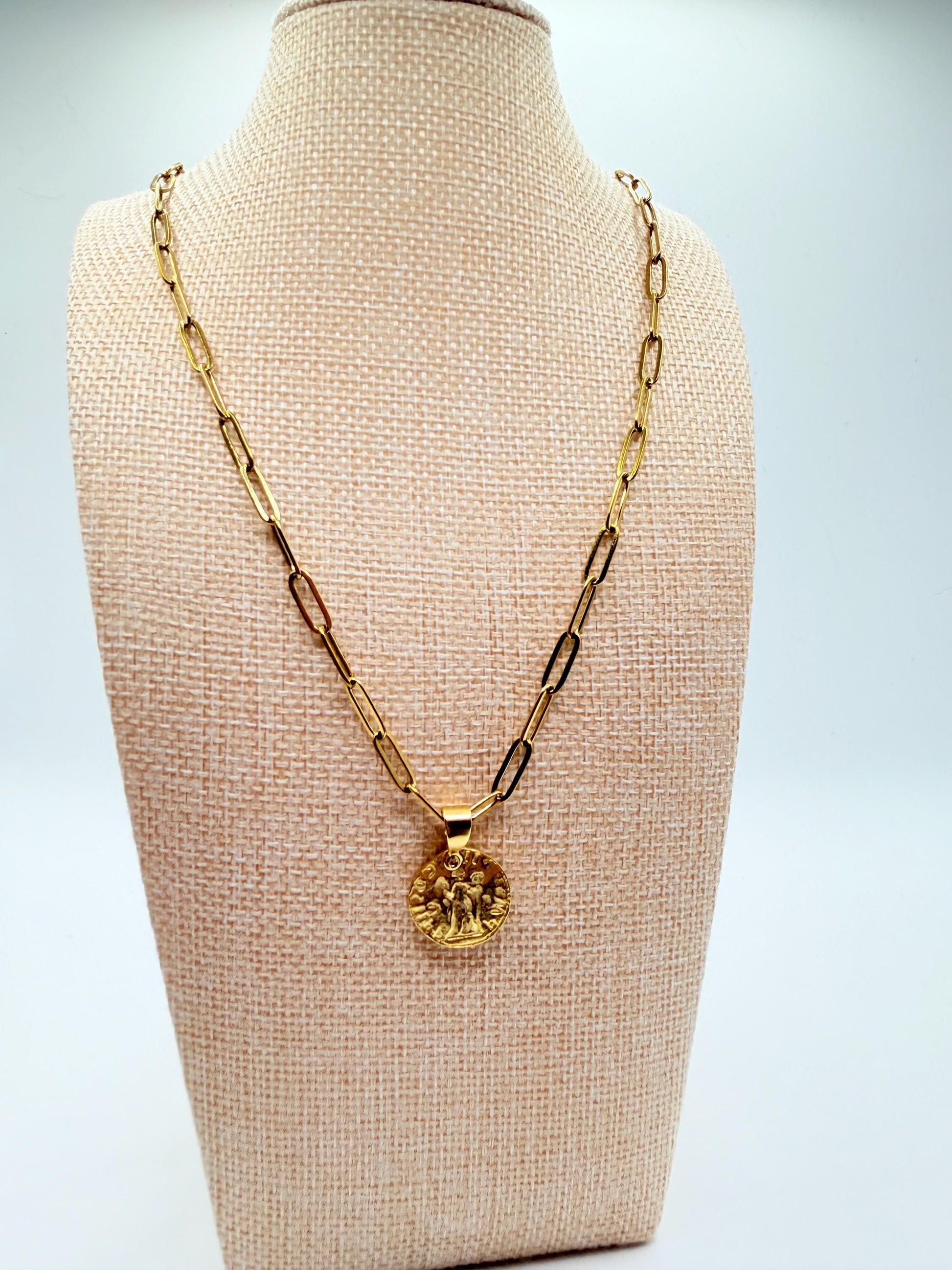 Gold necklace with a pendant on a beige mannequin bust against a light gray background