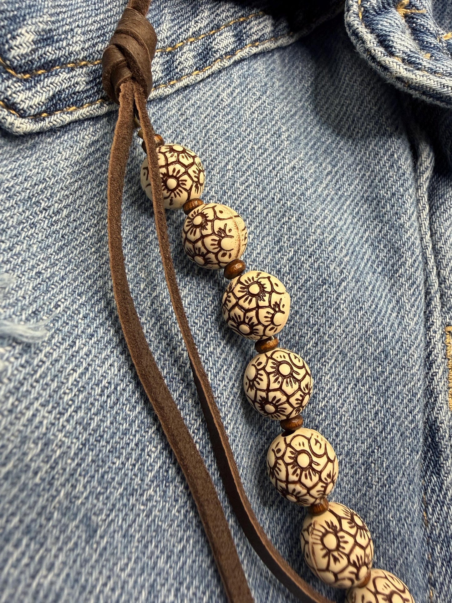 Bracelet with patterned beads on a brown cord against a denim background