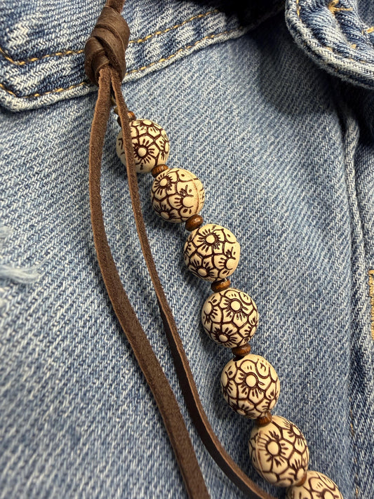 Bracelet with patterned beads on a brown cord against a denim background