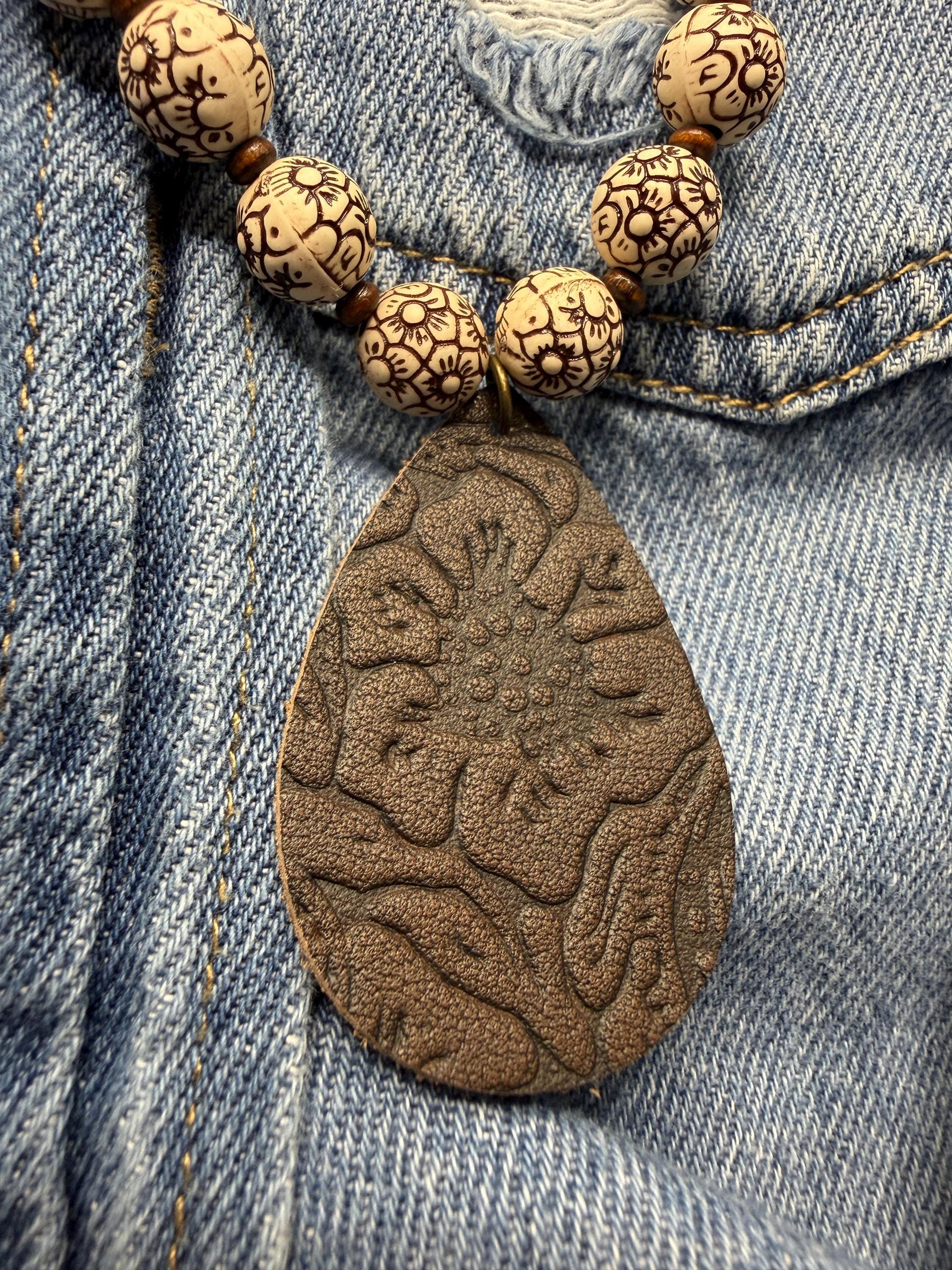 Necklace with wooden beads and a textured leather pendant on denim fabric