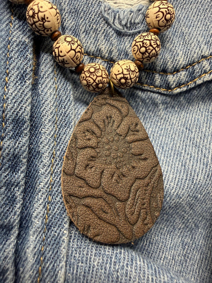 Necklace with wooden beads and a textured leather pendant on denim fabric