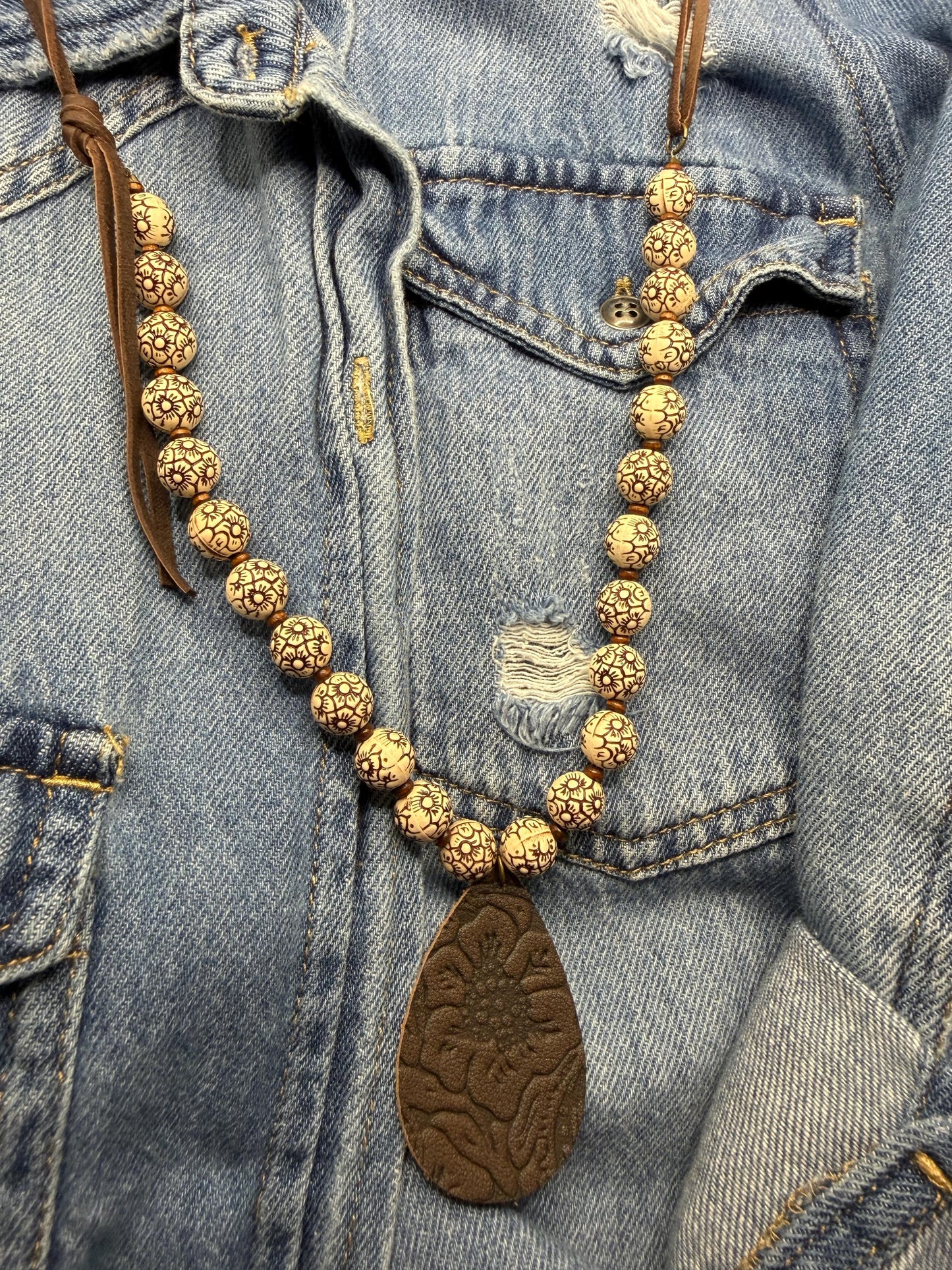 Gold beaded necklace with a brown leather pendant on a denim background
