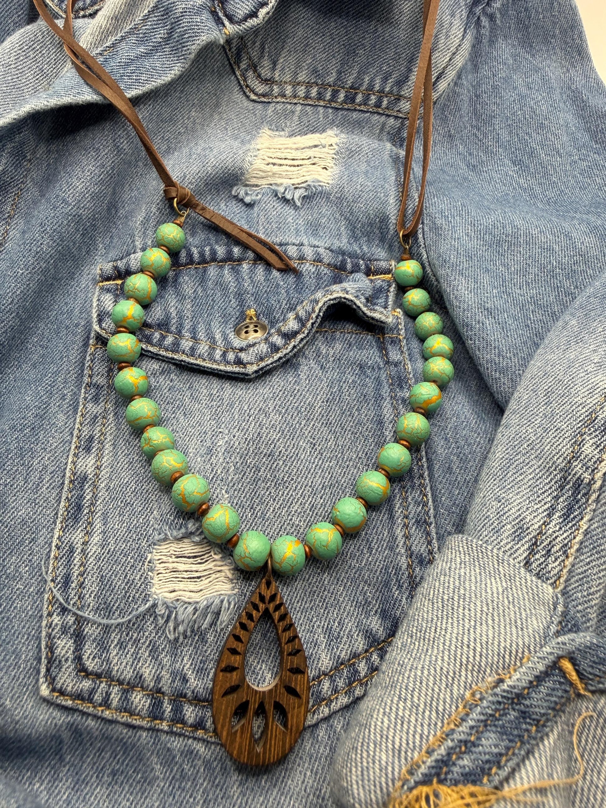 Necklace with green beads and wooden pendant on a denim background