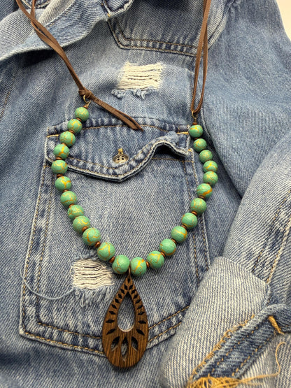 Necklace with green beads and wooden pendant on a denim background