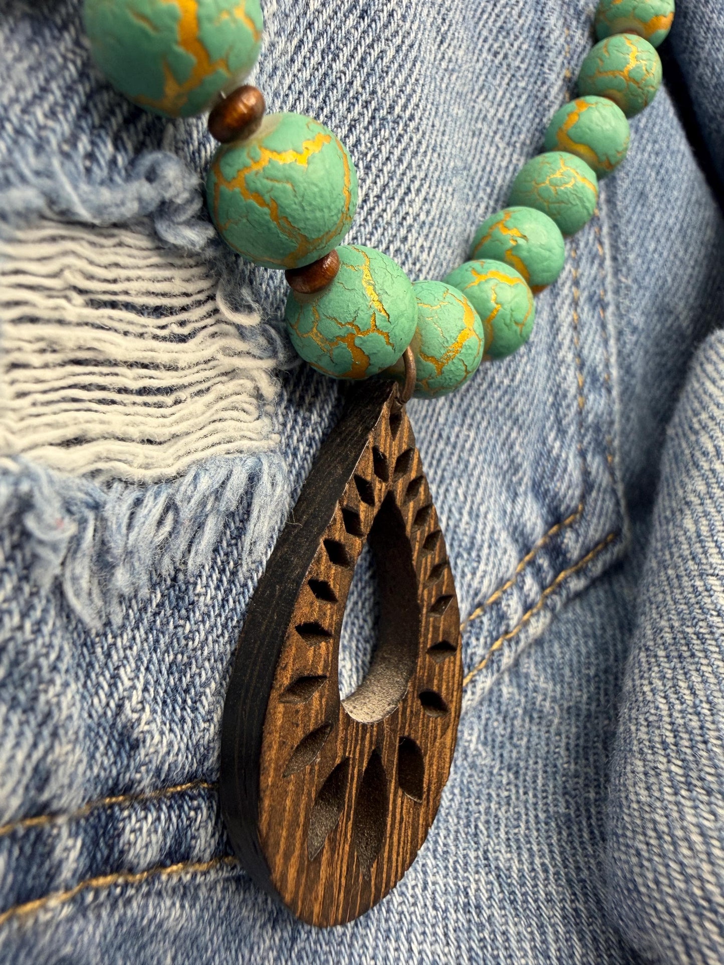 Necklace with green marbled beads and a wooden pendant on denim fabric