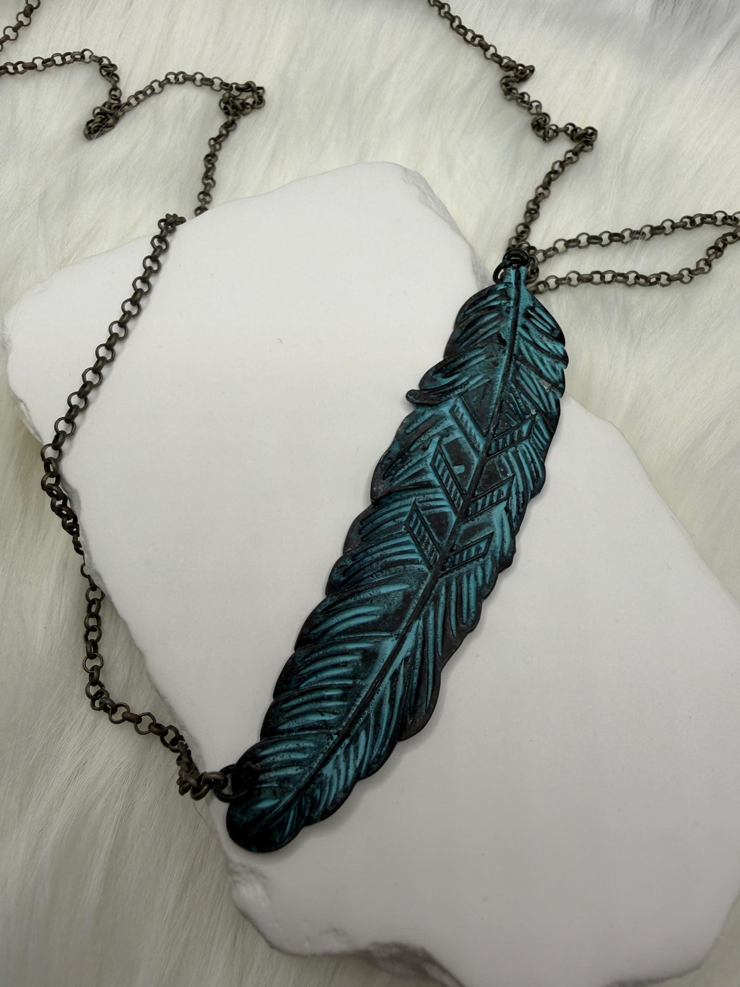 Feather-shaped pendant on a chain against a white background