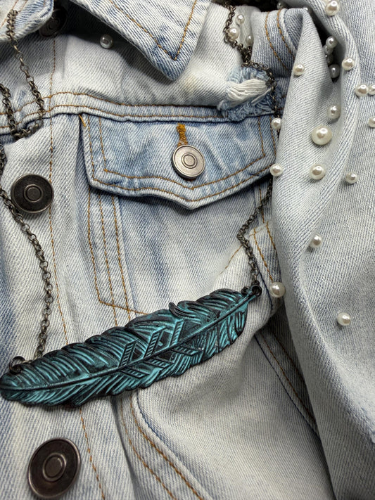 Close-up of a denim jacket with a turquoise feather pendant necklace.
