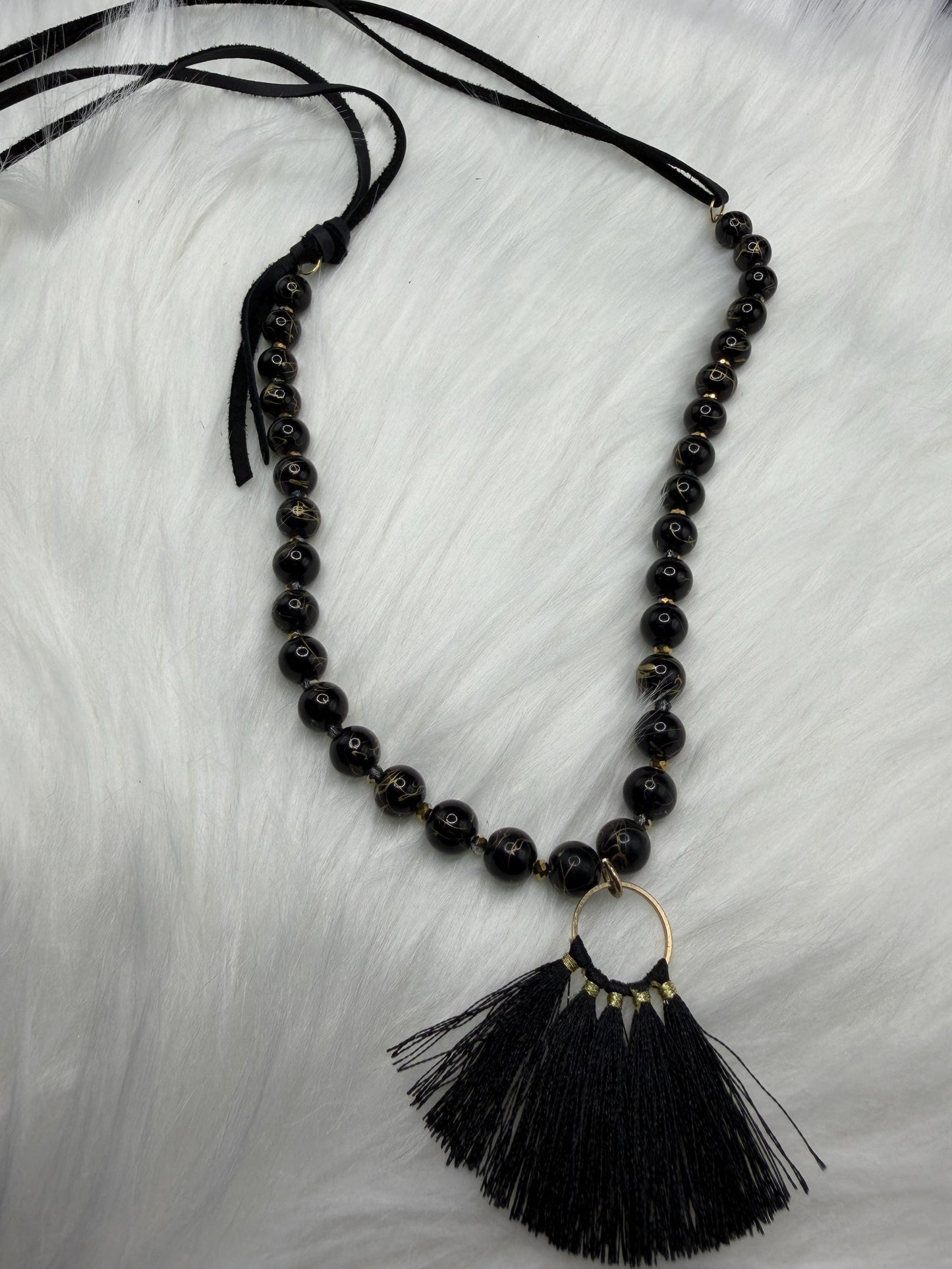 Black beaded necklace with a tassel pendant on a light gray background