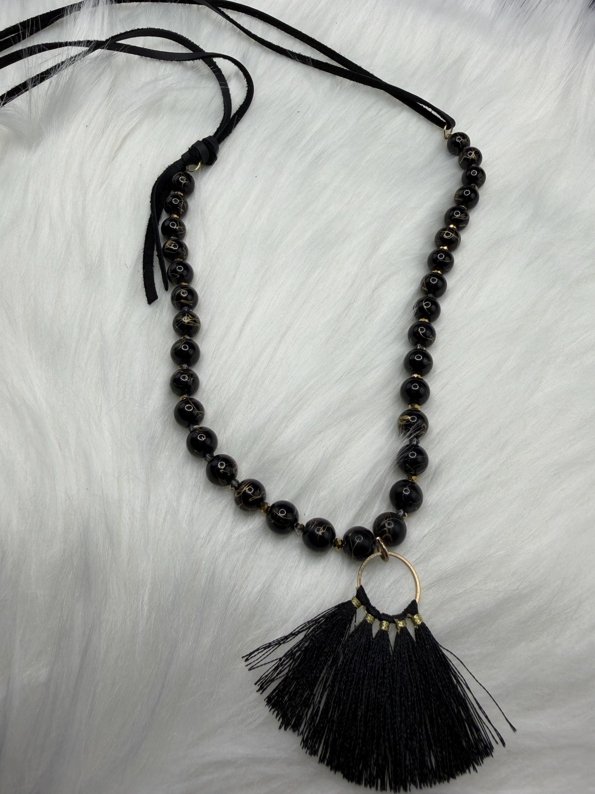 Black beaded necklace with a tassel pendant on a light gray background