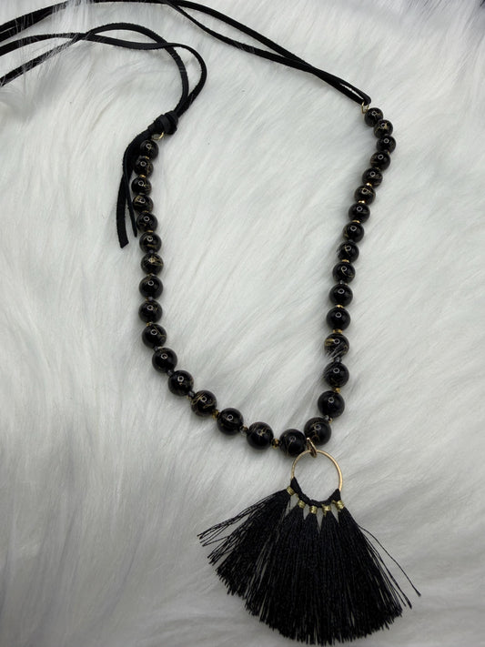 Black beaded necklace with a tassel pendant on a light gray background