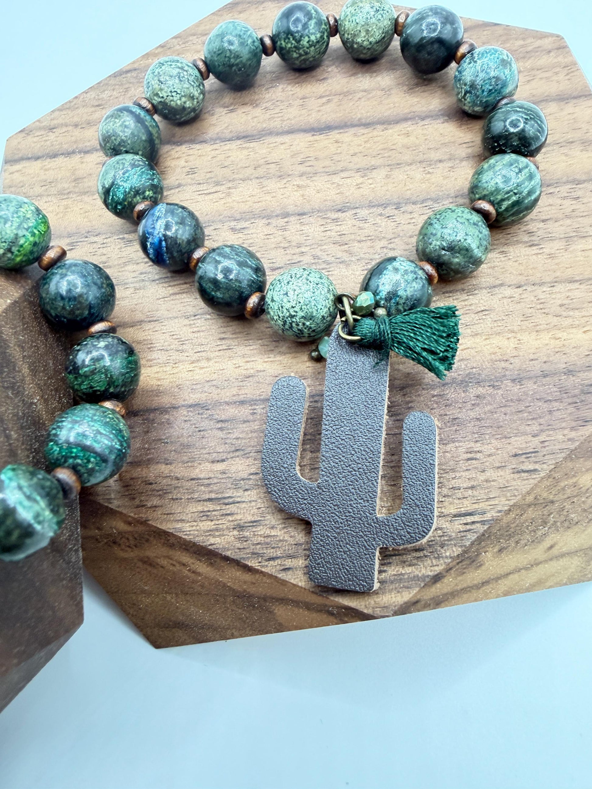 Green beaded bracelet with a cactus-shaped charm on a wooden stand.