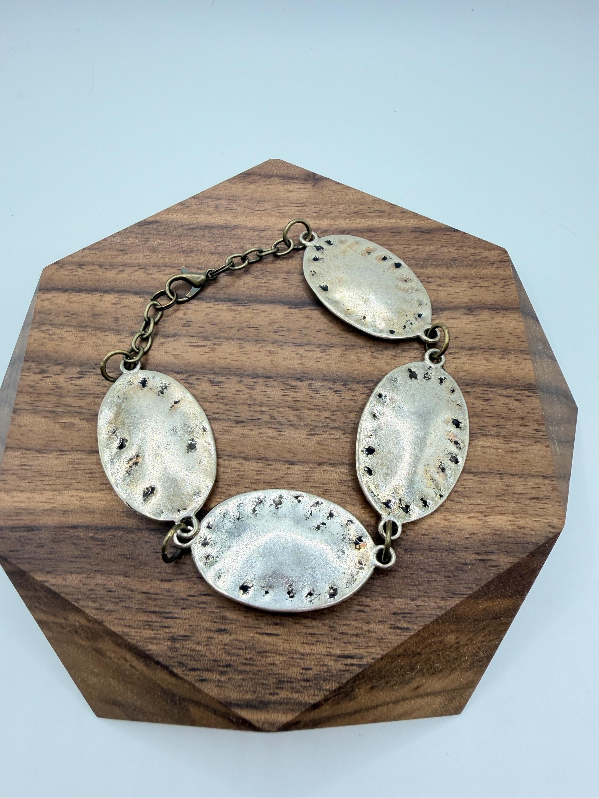 silver and bronze  bracelet  with oval pendants on a wooden stand against a light blue background