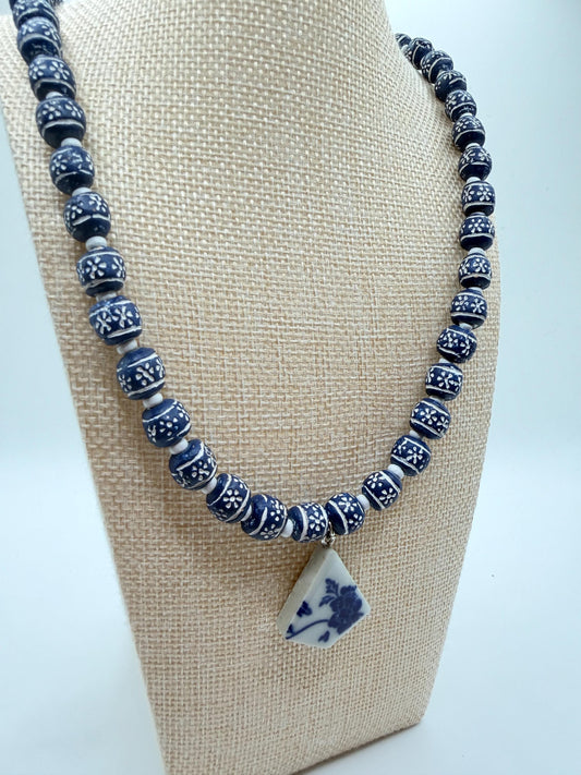 Blue and white beaded necklace on a beige display stand with a white background