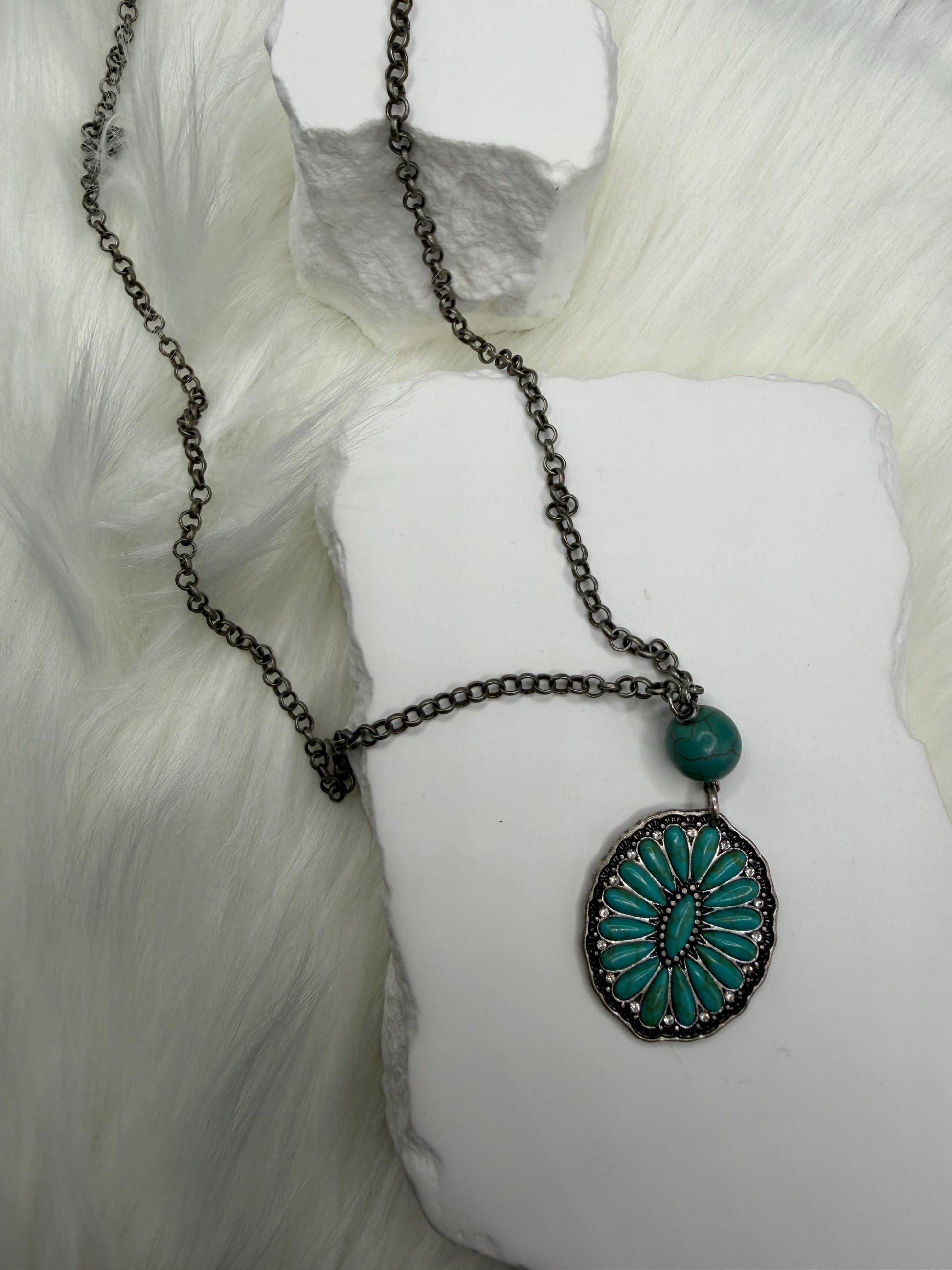 Necklace with a turquoise pendant on a white mannequin arm against a white background