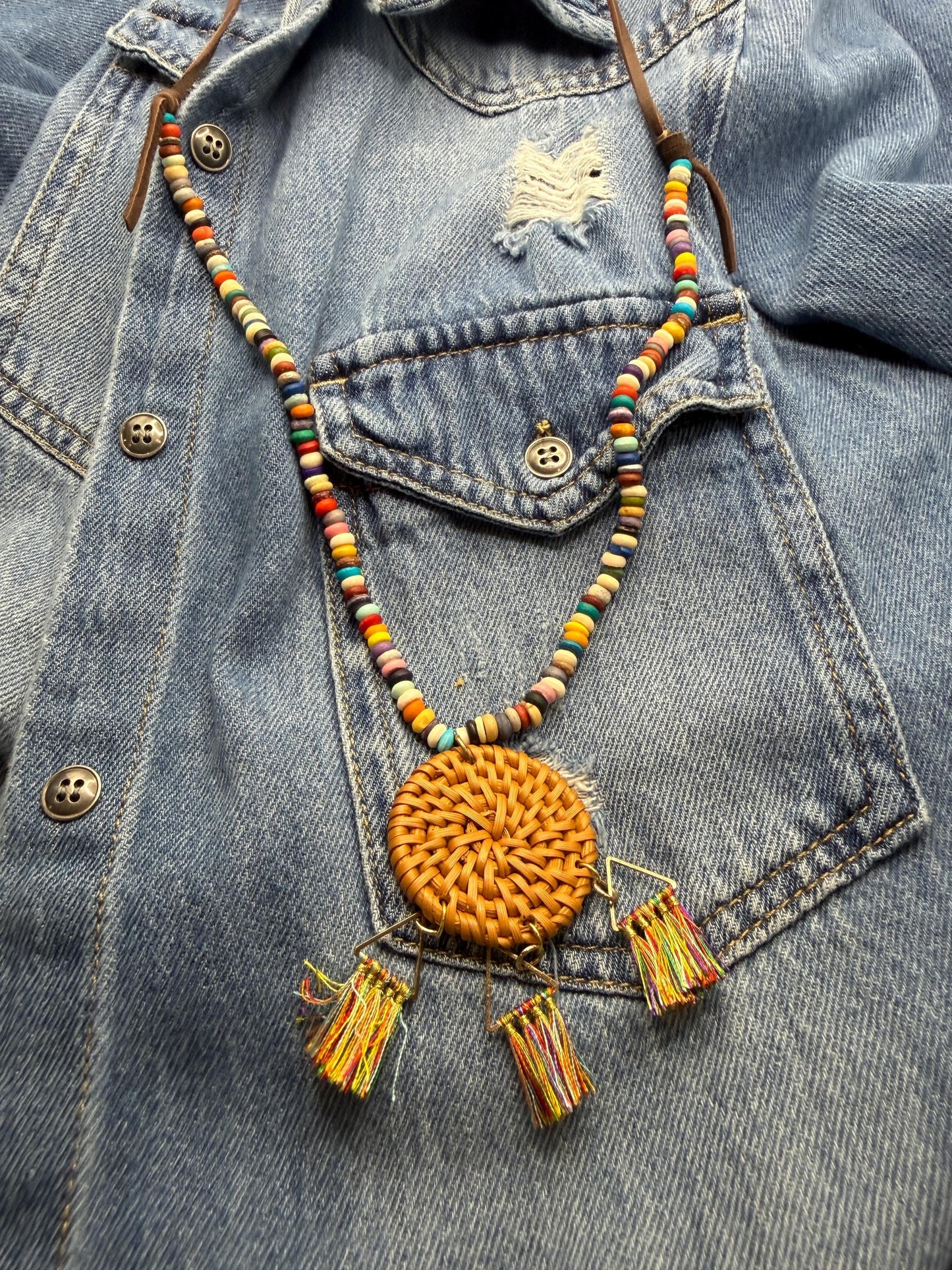 Colorful beaded necklace with a round orange pendant on a denim jacket.