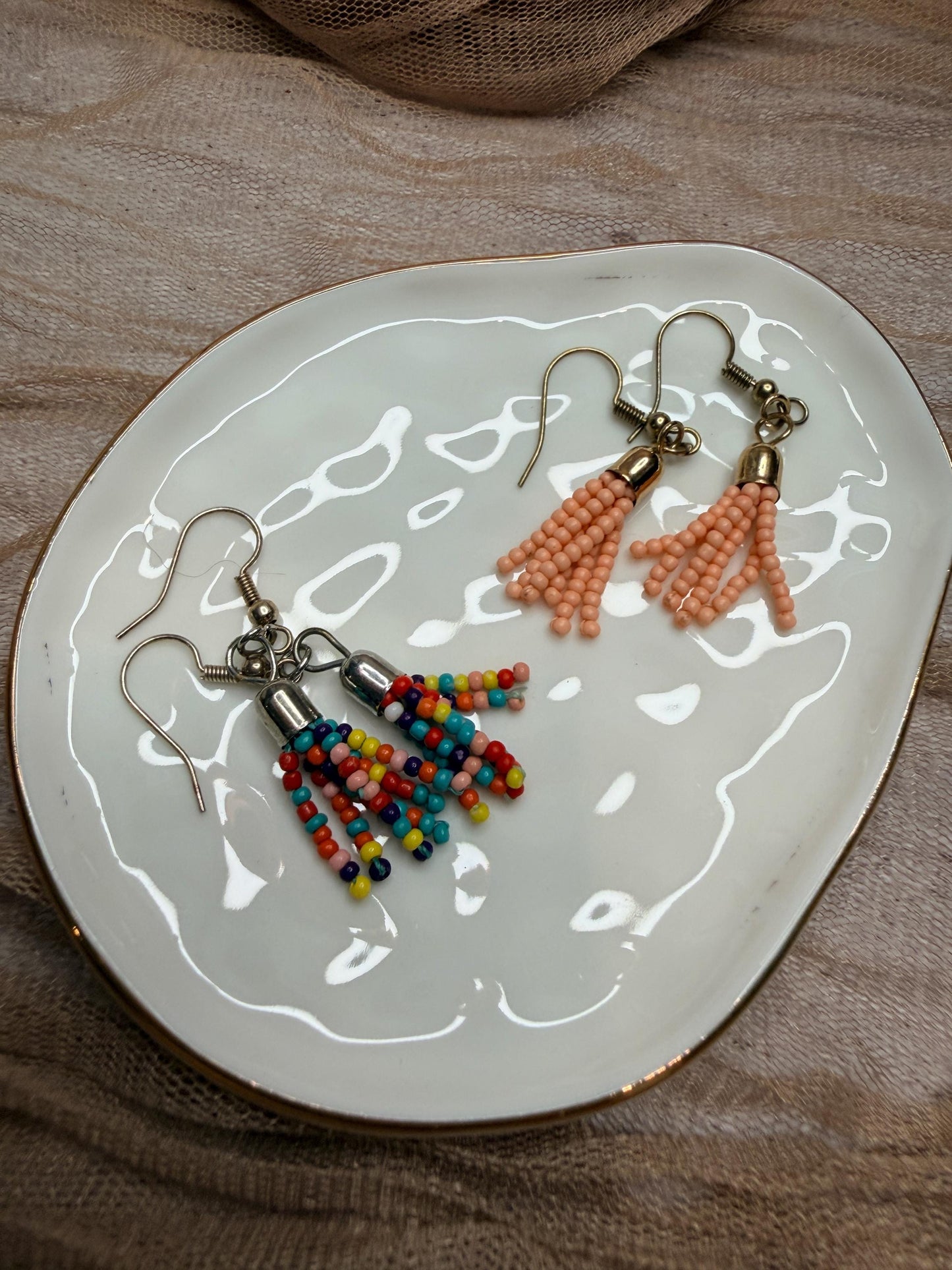 Two pairs of beaded earrings on a decorative plate.