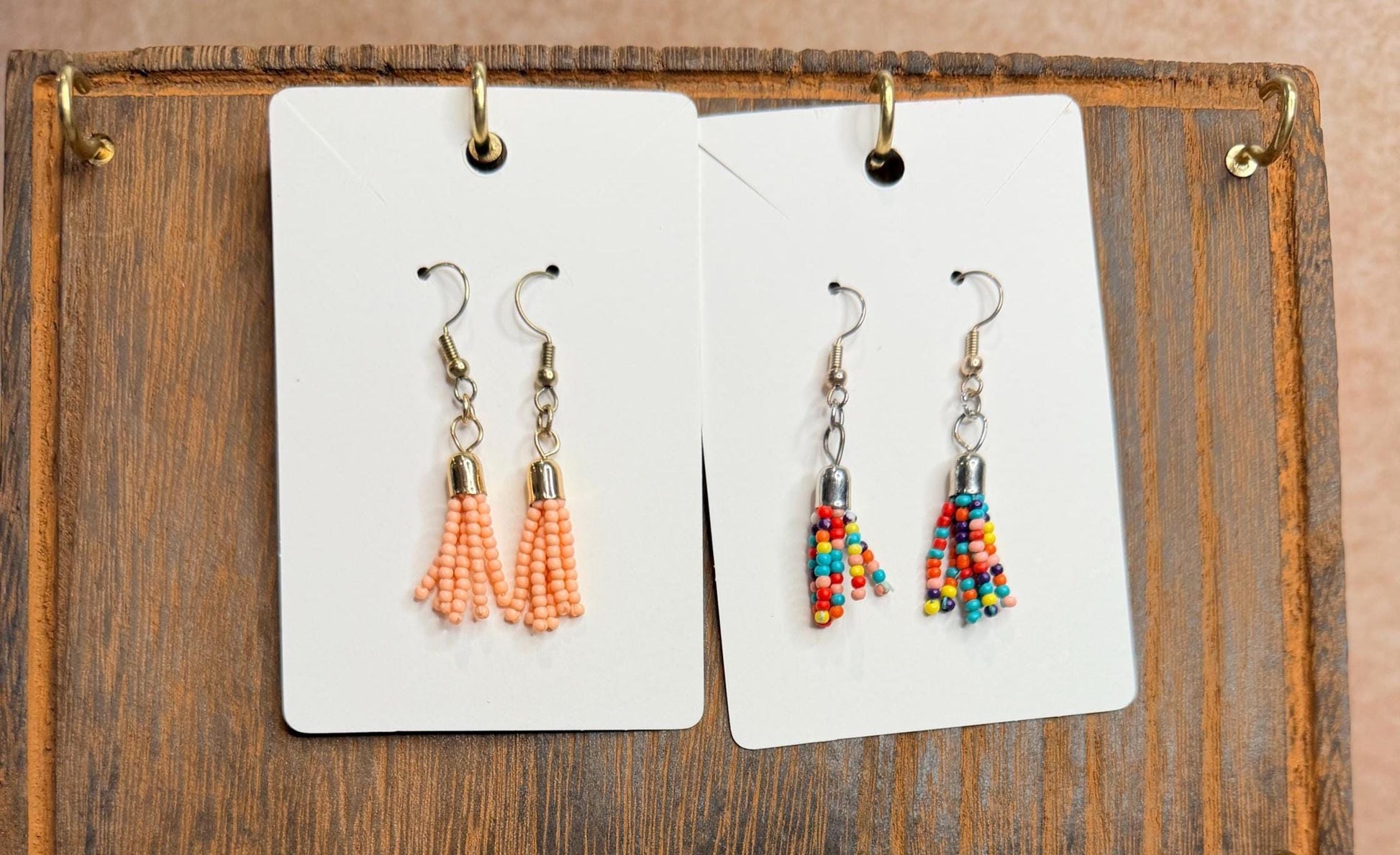 Two pairs of beaded earrings on display cards against a wooden background