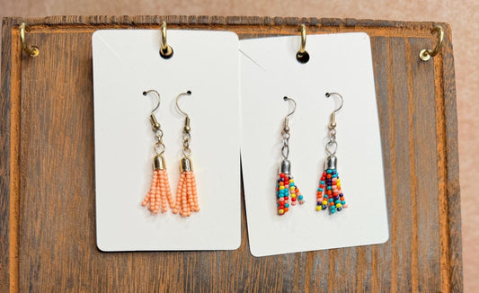 Two pairs of beaded earrings on display cards against a wooden background