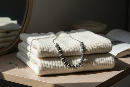 Stack of white folded sweaters with a necklace on top, placed on a wooden surface.