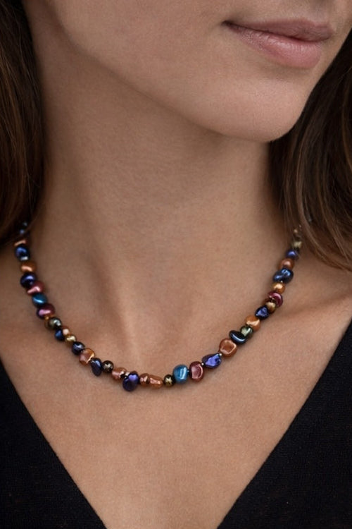 Close-up of a woman wearing a colorful pearl necklace against a neutral background