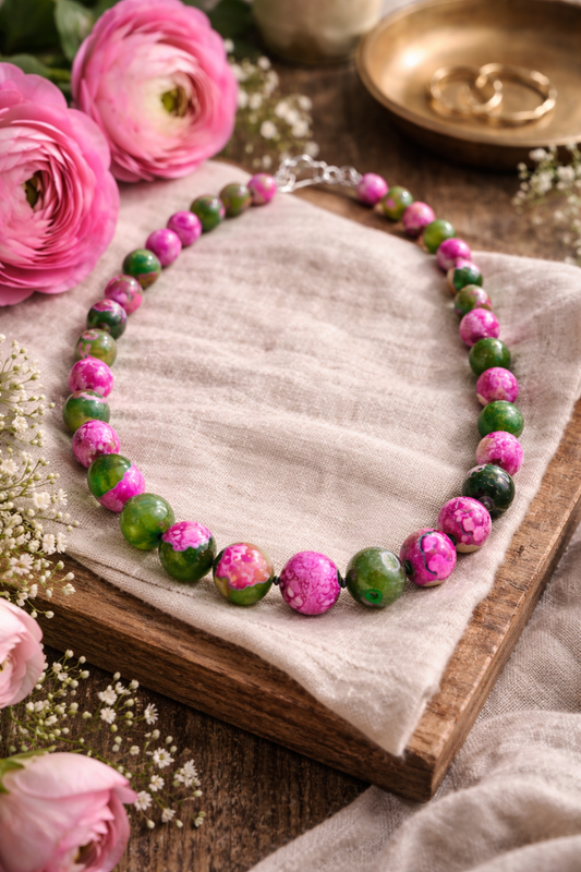 Necklace with pink and green beads on a wooden surface with pink flowers around